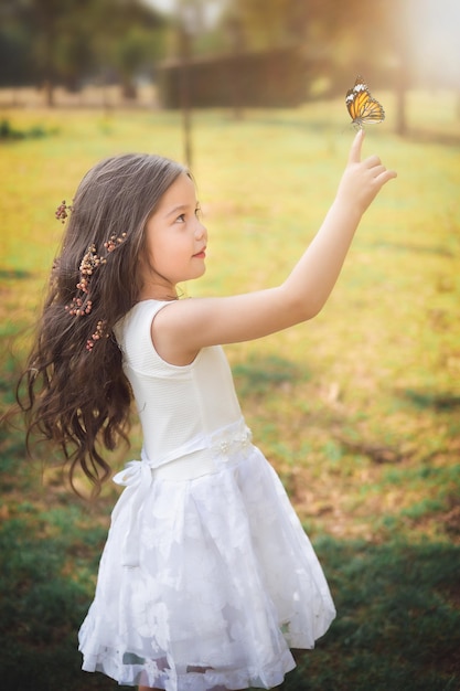 Mädchen im weißen Kleid wie eine Prinzessin, die mit einem Schmetterlings-Kopierraum-Kindertagsthema spielt