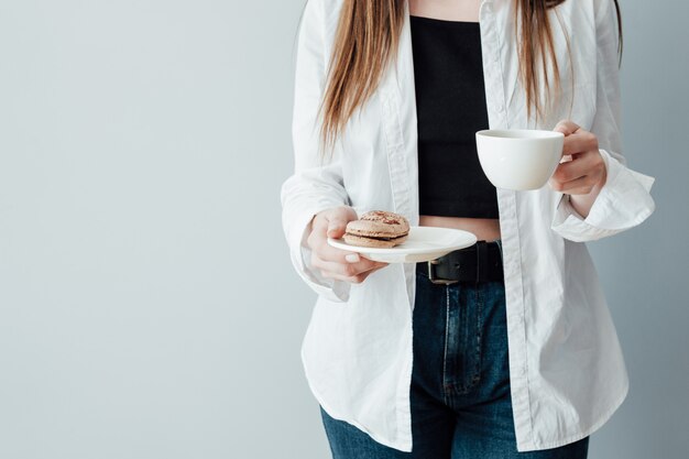 Mädchen im weißen T-Shirt und in der Jeans hält Tasse Kaffee und Teller