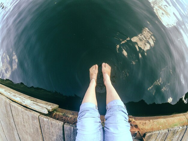 Mädchen in Blue Jeans sitzt an einem sonnigen Tag auf dem alten Kai im See. Kaukasisch.