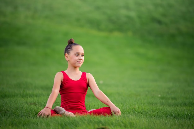 Mädchen in den leuchtend roten Overalls, die Gymnastik auf dem Gras im Park tun