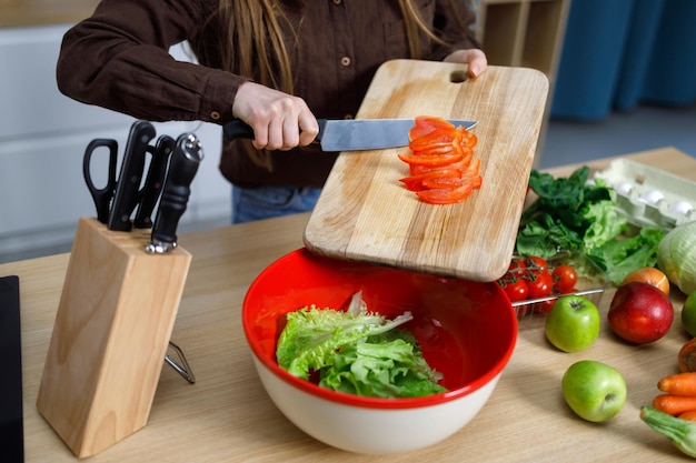 Mädchen in der Küche bereitet frischen Salat vor, schneidet Gemüse, wirft rote Paprika in die Schüssel