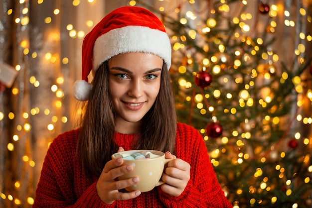 Mädchen in der roten Weihnachtsmütze mit einer Tasse heißem Kakao