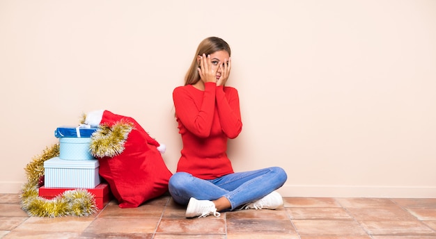 Mädchen in die Weihnachtsfeiertage, die auf den Bodenbelagaugen sitzen und durch Finger schauen