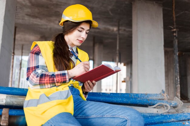 Mädchen in einem Bauhelm und einer Weste schreibt in ein Notizbuch auf einer Baustelle