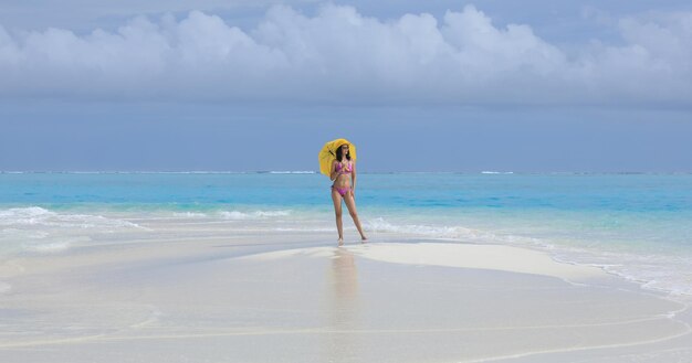 Mädchen in einem Bikini mit einem gelben Regenschirm auf dem Meeressand