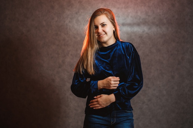 Mädchen in einem blauen Pullover auf grauem Hintergrund. Habe schöne Haare und sie posiert wunderschön