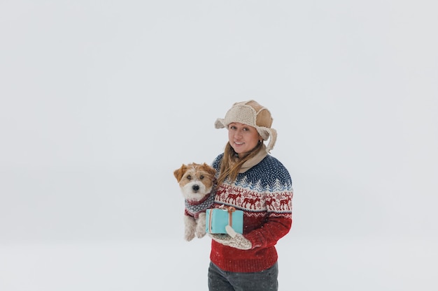 Mädchen in einem braunen Mantel gibt einem Jack Russell Terrier ein Geschenk auf weißem Hintergrund während eines Schneesturms Der Hund sitzt auf den Händen eines Mannes Weihnachtskonzept