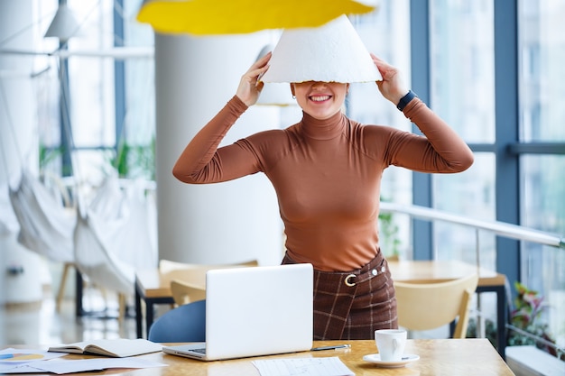 Mädchen in einem Café steht an einem Holztisch und lächelt und albert mit Kaffee herum und spielt mit einer Lampe