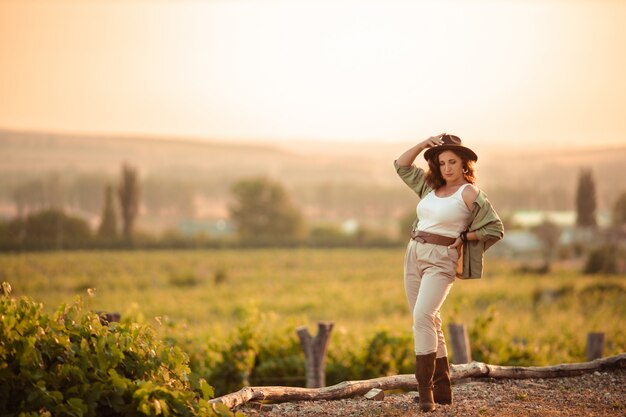 Mädchen in einem Cowboyhut bei Sonnenuntergang in der Landschaft in den Weinbergen.