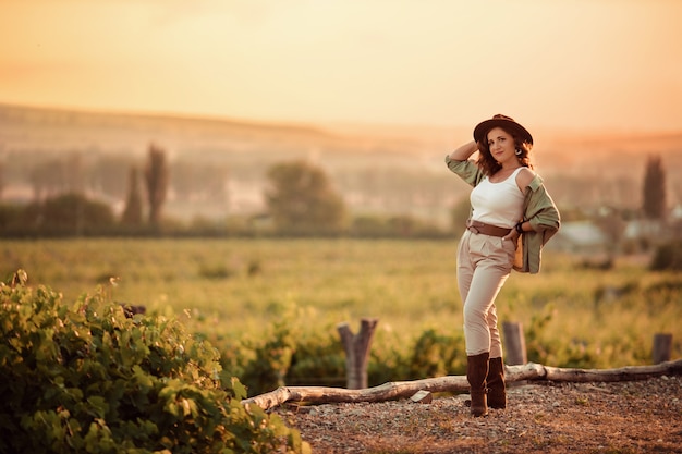 Mädchen in einem Cowboyhut bei Sonnenuntergang in der Landschaft in den Weinbergen.