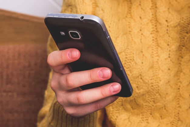 Mädchen in einem gelben Pullover hält ein schwarzes Handy