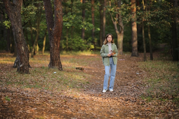 Mädchen in einem grünen Hemd und Blue Jeans im Herbstwald Mädchen, das ein Ahornblatt in ihren Händen hält