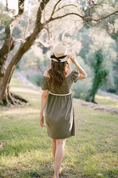 Mädchen in einem grünen Kleid und Hut geht einen grünen Rasen unter einer Baumrückansicht entlang