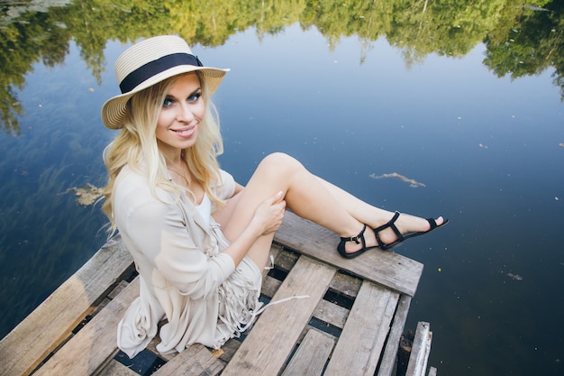 Mädchen in einem Hut, der auf dem Herbstsee auf der Brücke ruht