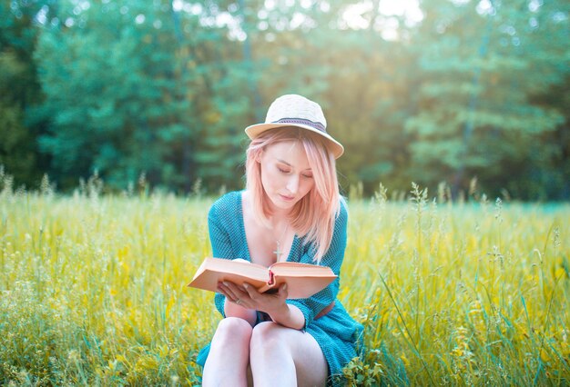 Mädchen in einem Hut liest ein Buch an der frischen Luft.