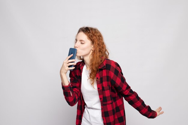 Mädchen in einem karierten Hemd auf hellem Hintergrund mit einem Smartphone