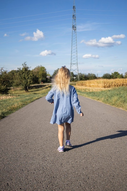 Mädchen in einem Kleid, das mit dem Rücken entlang der Straße auf dem Feld läuft