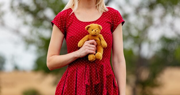 Mädchen in einem Kleid in Tupfen mit Teddybär auf Landstraße