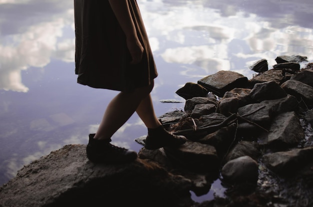 Mädchen in einem Kleid und Turnschuhen, das auf den Felsen am See spaziert