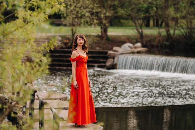 Mädchen in einem langen roten Kleid nahe dem See im Park bei Sonnenuntergang.