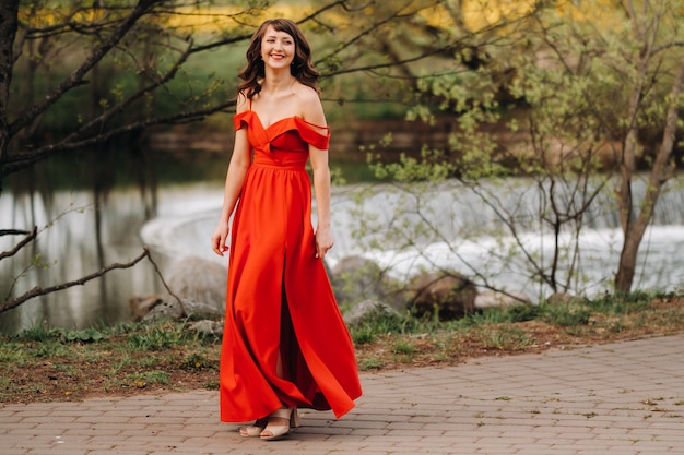 Mädchen in einem langen roten Kleid nahe dem See im Park bei Sonnenuntergang.