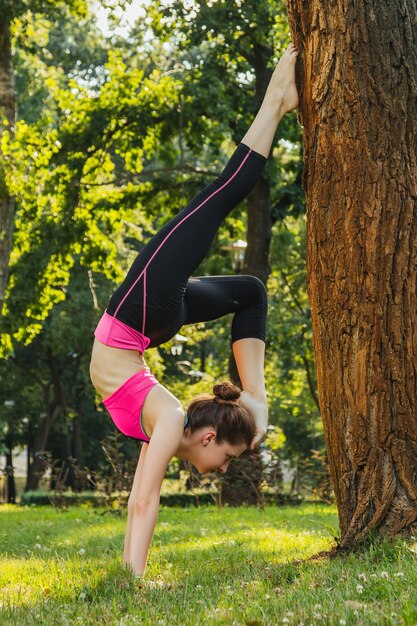 Mädchen in einem leichten Trainingsanzug, der nachmittags im Sommer Yoga im Park macht