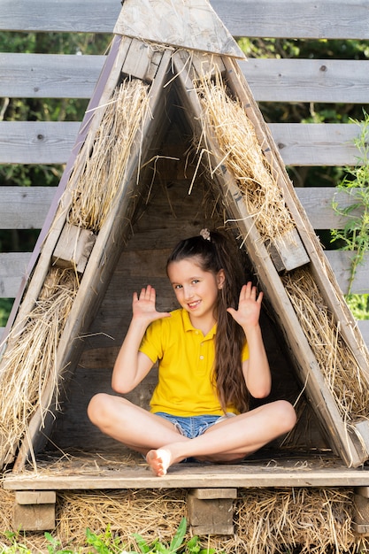 Mädchen in einem leuchtend gelben T-Shirt sitzt in einer kleinen Hütte