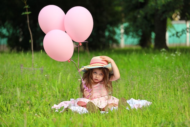 Mädchen in einem rosa Kleid mit Hut sitzt auf dem Gras im Park. Foto in hoher Qualität