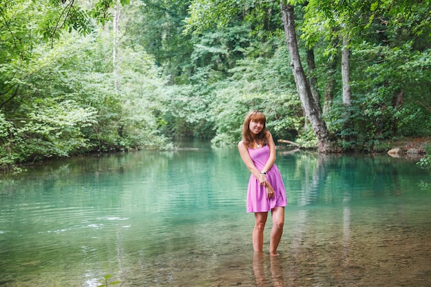 Mädchen in einem rosa kurzen Kleid geht auf einen Fluss im Wald