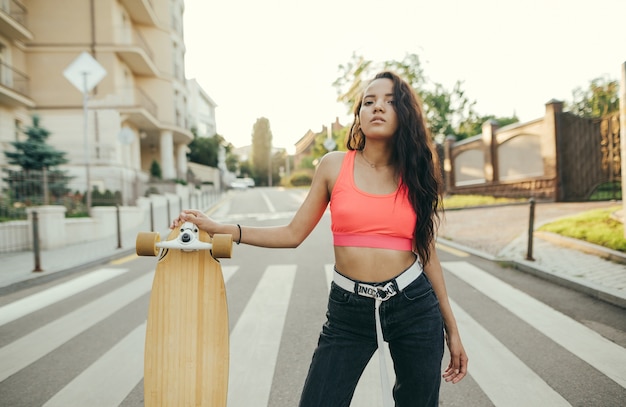 Mädchen in einem rosa T-Shirt und Jeans steht auf der Straße mit einem Longboard