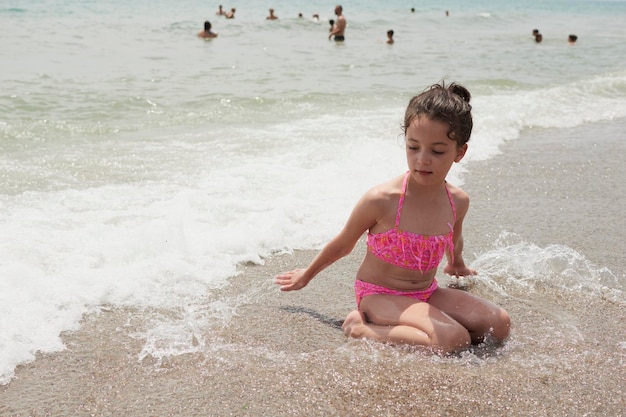Mädchen in einem rosafarbenen Bikini, das an einem sonnigen Sommertag glücklich am Ufer des Strandes mit den Wellen spielt Vera Spanien
