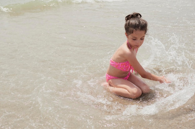 Mädchen in einem rosafarbenen Bikini, das an einem sonnigen Sommertag glücklich am Ufer des Strandes mit den Wellen spielt Vera Spanien