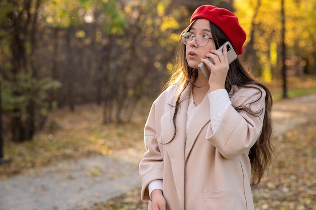 Mädchen in einem roten Barett, das im Herbstpark auf dem Handy anruft