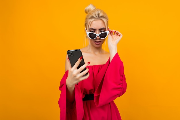 Mädchen in einem roten Kleid hält Brille auf ihrem Gesicht, während ein Telefon an einer gelben Wand hält