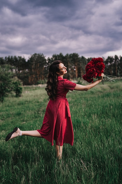 Mädchen in einem roten Kleid mit Pfingstrosen im Wald