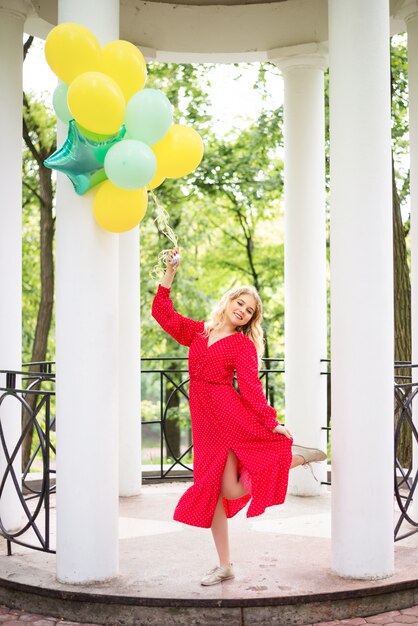 Mädchen in einem roten Kleid und einem Bündel bunter Luftballons im Park