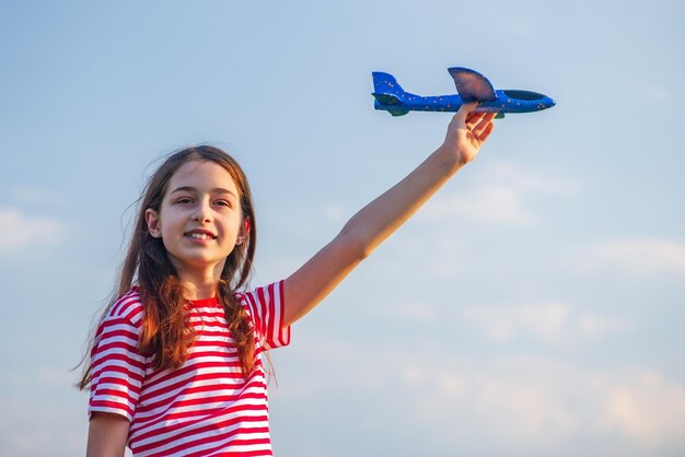 Mädchen in einem roten T-Shirt mit einem weißen Streifen Ein junges Mädchen mit einem blauen Spielzeugflugzeug in ihren Händen gegen den Himmel