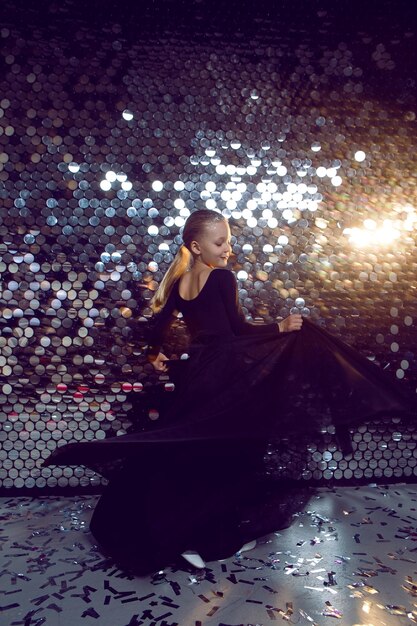 Foto mädchen in einem schwarzen kleid tanzt im studio auf einem hintergrund mit pailletten