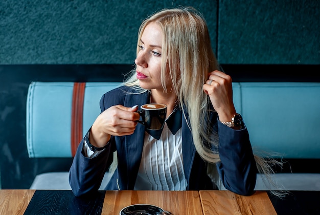 Mädchen in einem strengen Anzug in einem Café, das Kaffee trinkt