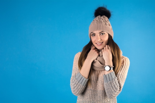 Mädchen in einem warmen Pullover, Schal und Mütze auf einem blauen Hintergrund