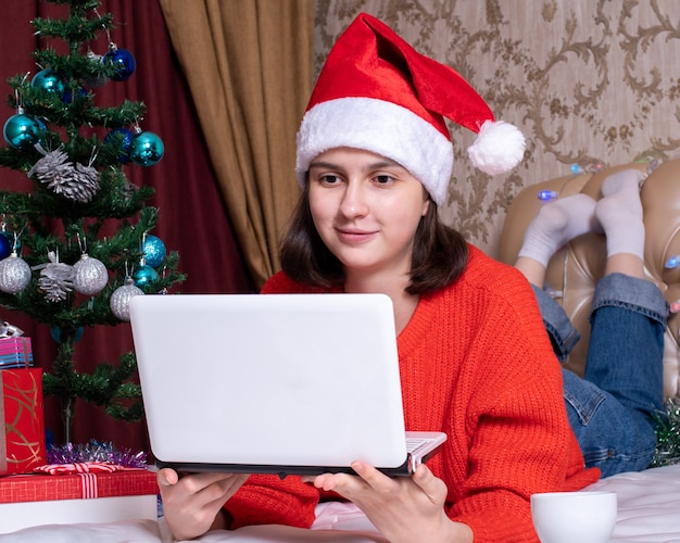 Mädchen in einem Weihnachtsmannhut hält einen Laptop auf dem Bett