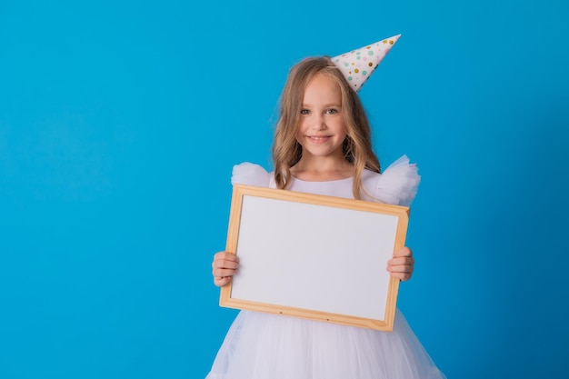 Mädchen in einem weißen, flauschigen, eleganten Kleid hält eine weiße Schreibtafel in ihren Händen