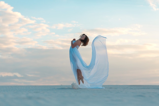 Mädchen in einem weißen Kleid der Fliege tanzt und wirft im Sand auf