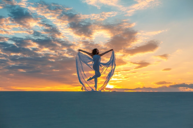 Mädchen in einem weißen kleid der fliege tanzt und wirft in der sandwüste bei sonnenuntergang auf