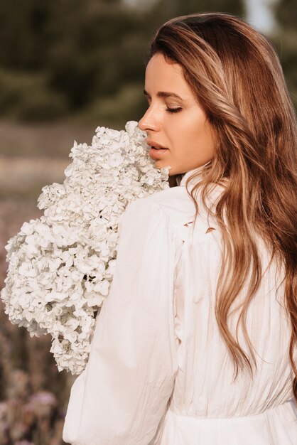 Mädchen in einem weißen Kleid mit einem Blumenstrauß im Sommer