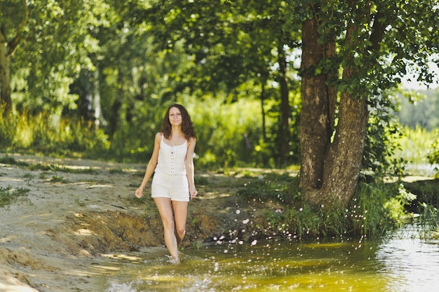 Mädchen in einem weißen kurzen Kleid geht am Ufer des Teiches 6333 entlang