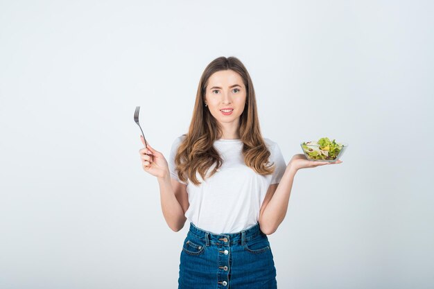 mädchen in einem weißen t-shirt hält eine schüssel salat in den händen und isst