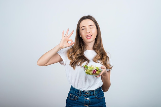 mädchen in einem weißen t-shirt hält eine schüssel salat in den händen und isst