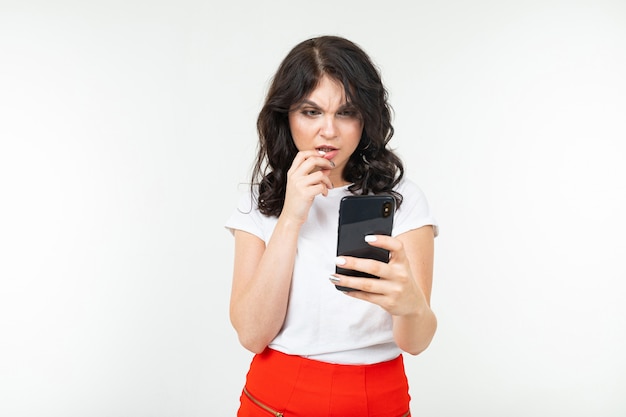 Mädchen in einem weißen T-Shirt liest nachdenklich eine Nachricht auf ihrem Smartphone auf einem weißen Studio mit Kopierraum