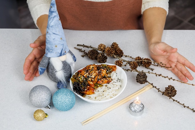 Mädchen in einer braunen Schürze Platte mit Reisnudeln und Hähnchen Festliche Dekoration Dunkler Hintergrund der Küche zu Hause Weihnachtskonzept